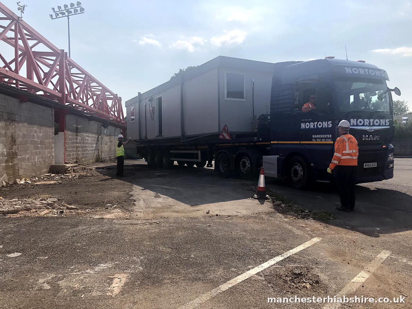 Articulated HIAB carrying a large grey cabin with two banksmen alongside