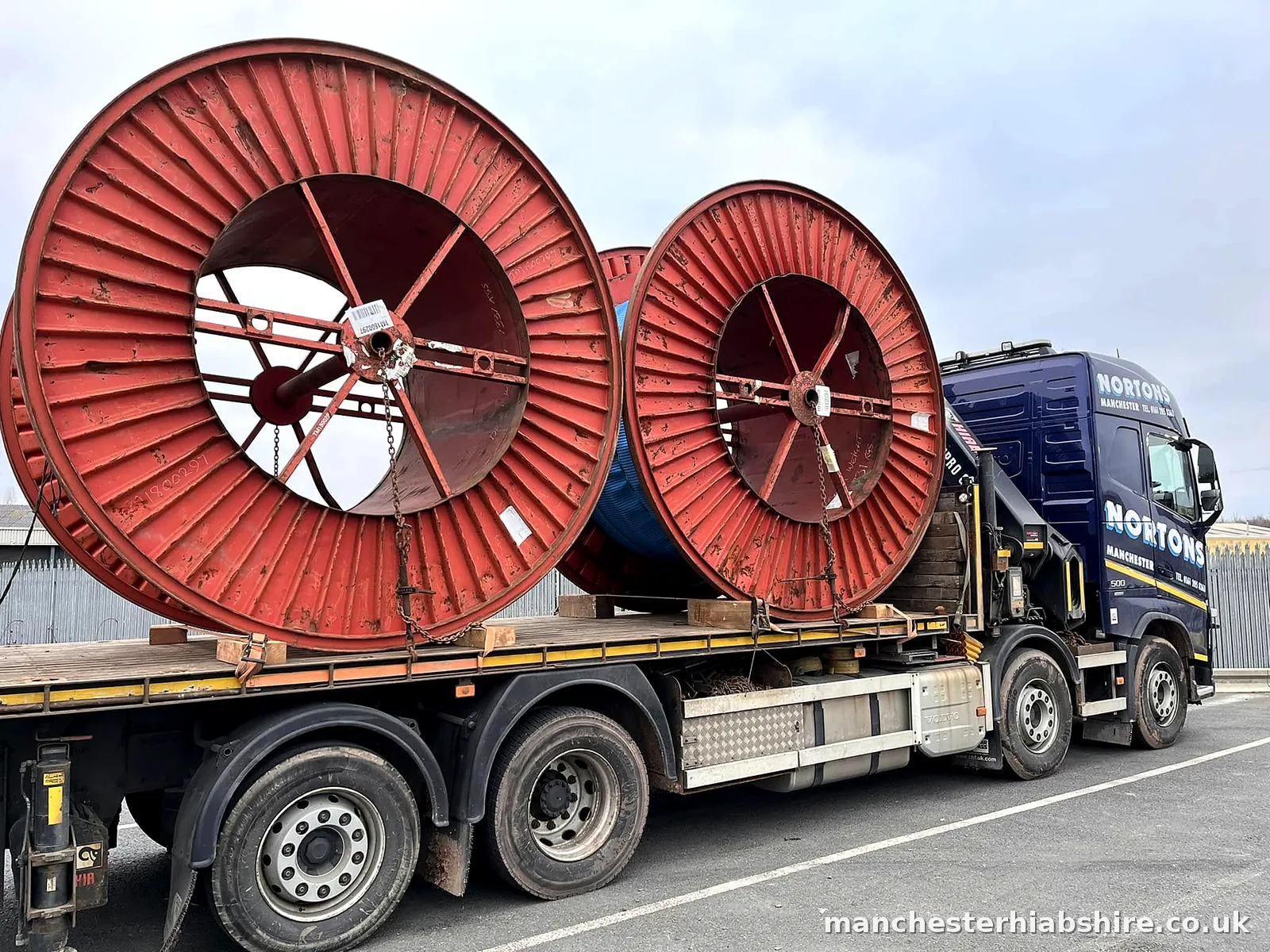 Flatbed carrying two large steel cable drums chained to the bed