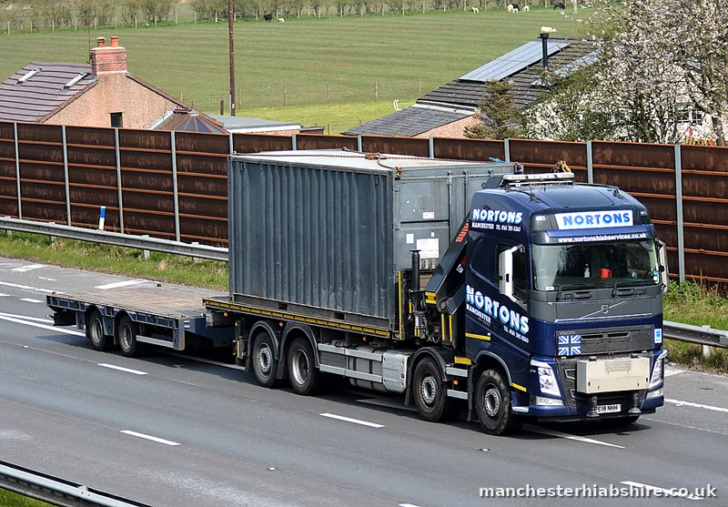 Grey container carried on a HIAB lorry past houses