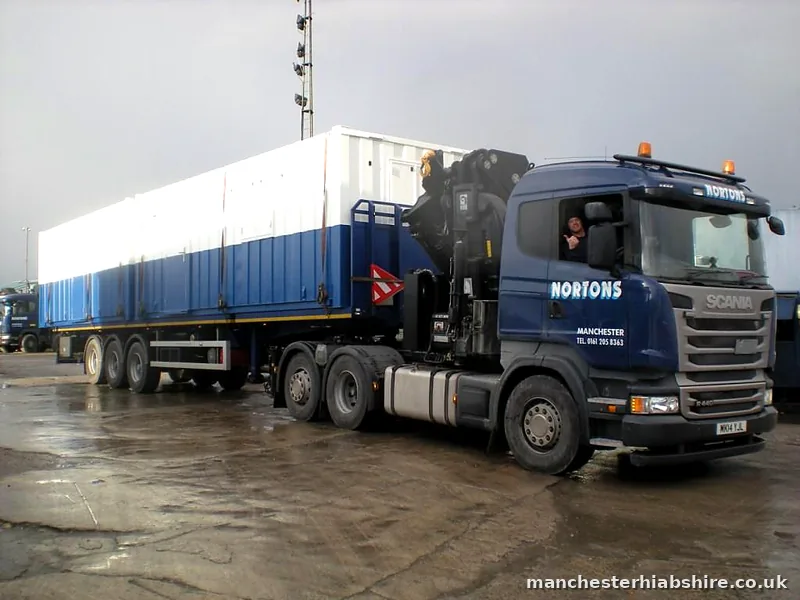 Driver leaning from the cab of a HIAB lorry hauling a long modular unit