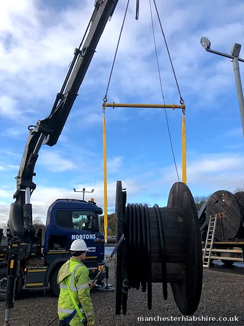 Spreader beam and slings lifting a cable drum with a banksman on the tagline
