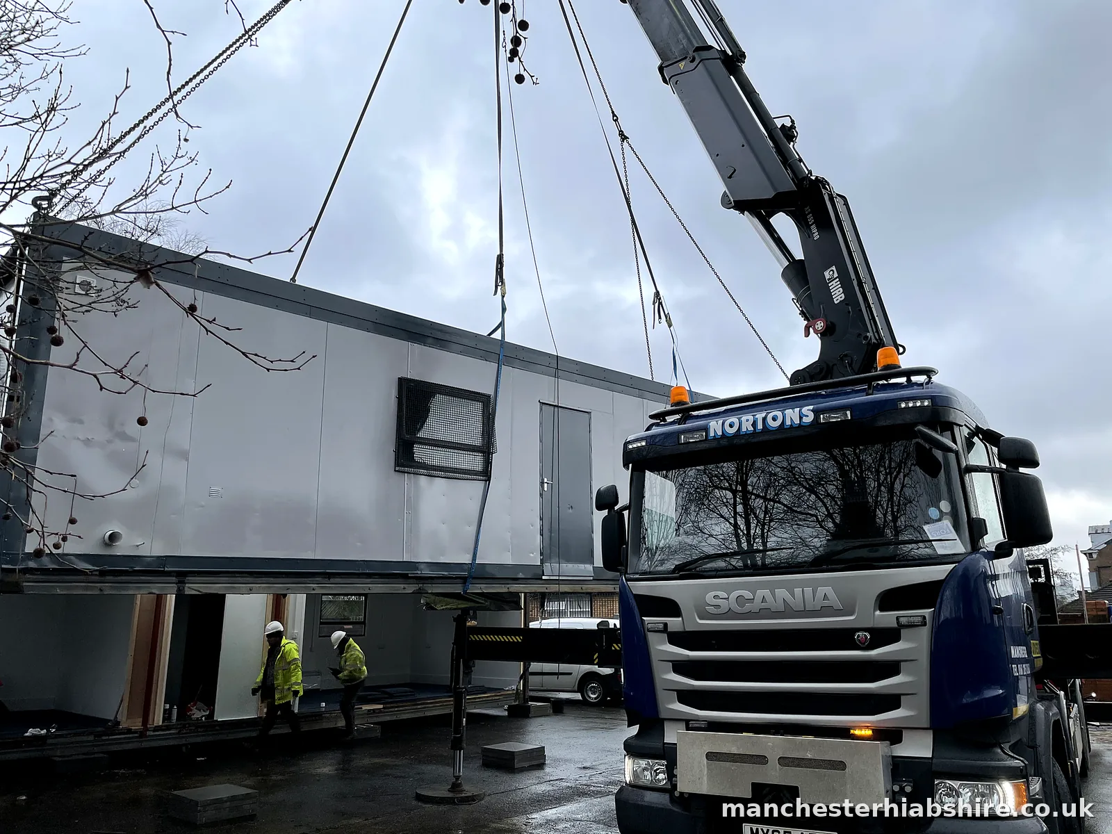 Modular building unit being chain lifted into place with two crew in hard hats