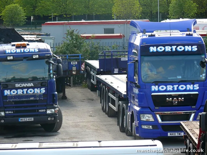 Two HIAB tractor units nose on in the secure yard with flat trailers behind