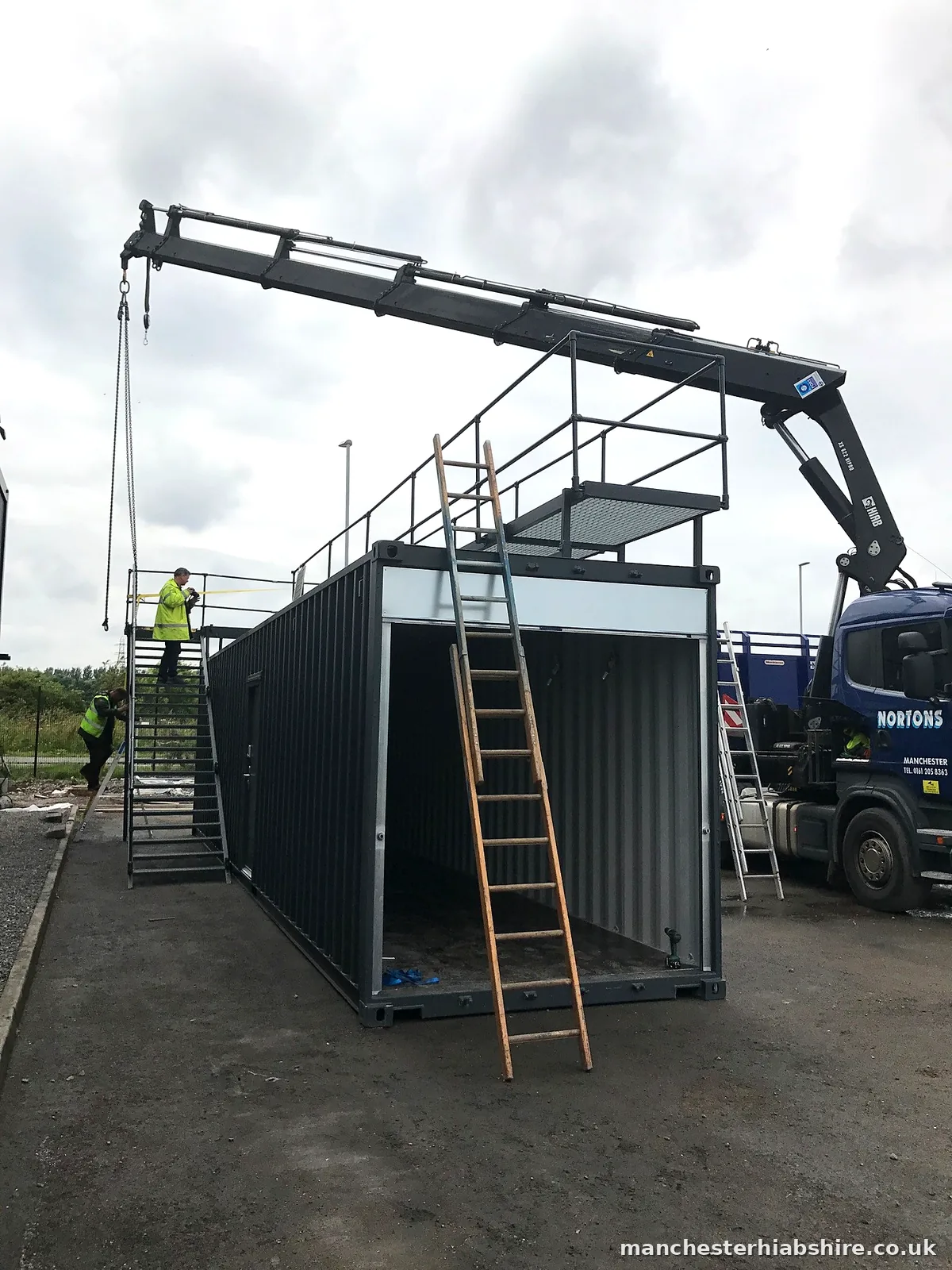 Shipping container fitted with an external staircase being lifted on chains