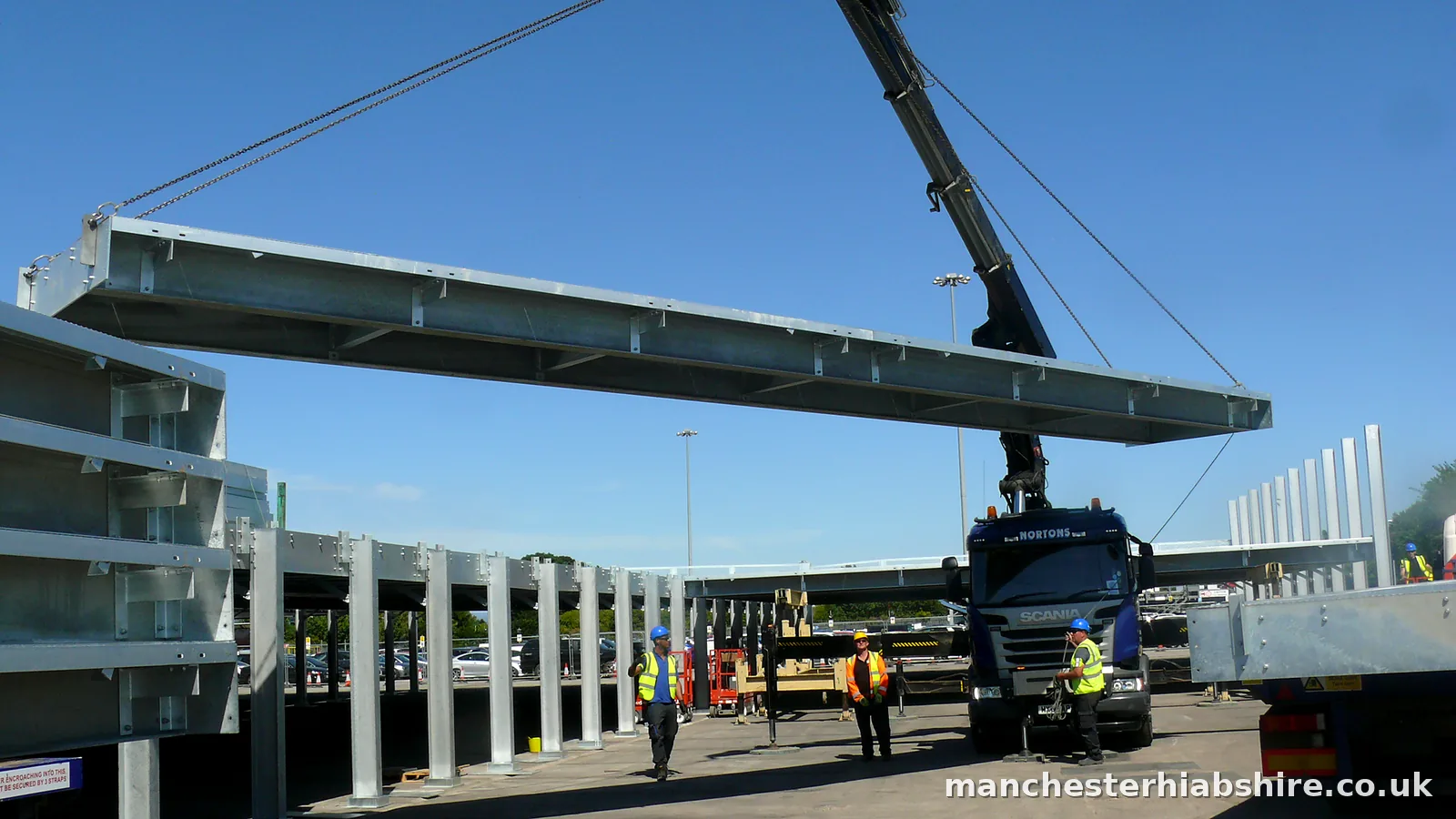 HIAB lifting a long galvanised steel beam into a canopy frame with three crew