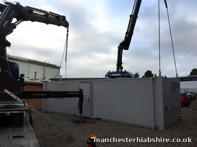 Two HIAB lorries setting a long cabin down onto gravel