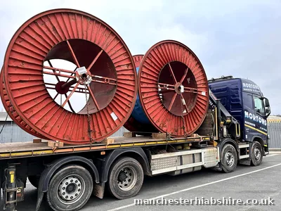 Flatbed carrying two large steel cable drums chained to the bed