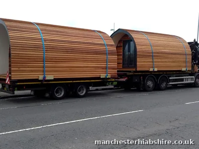 Two cedar clad glamping pods loaded on the lorry and trailer, side profile