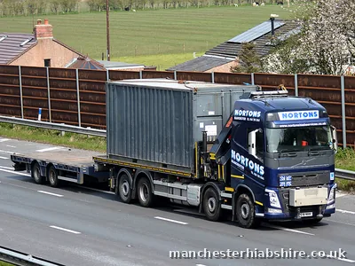 Grey container carried on a HIAB lorry past houses