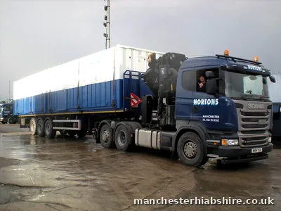 Driver leaning from the cab of a HIAB lorry hauling a long modular unit