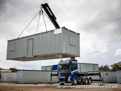 Lorry mounted crane lifting a portable site cabin clear of the flatbed