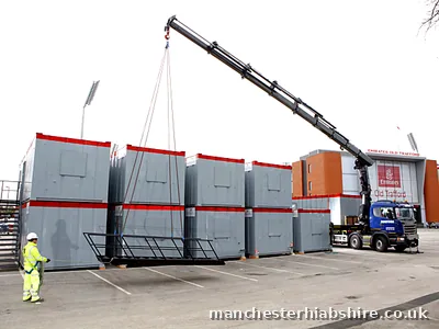 Steel access staircase lifted on the HIAB beside stacked modular units at Emirates Old Trafford