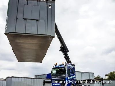 Site cabin lifted high and tilted on the HIAB crane above the lorry