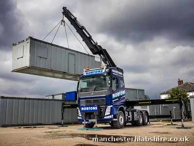 Lorry mounted crane holding a site cabin level under heavy cloud