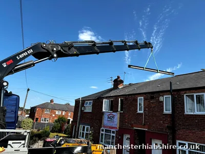 Lorry mounted crane lifting a beam over houses