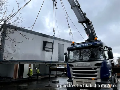 Modular building unit being chain lifted into place with two crew in hard hats