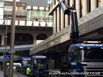 Two HIAB lorries on a closed city street with the boom reaching over a concrete podium