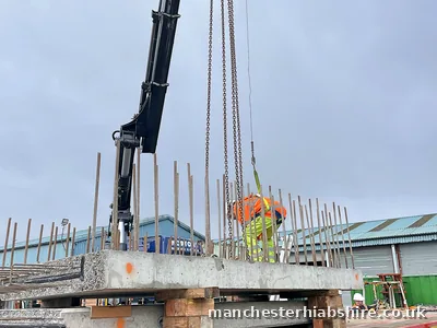 Precast concrete plank being lifted on chains with a banksman guiding the load