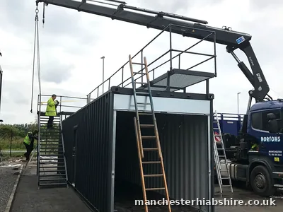 Shipping container fitted with an external staircase being lifted on chains