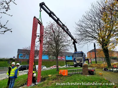 Brick effect entrance sign installed on the HIAB crane with crew guiding it into position