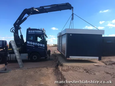 Dark modular unit lifted on the HIAB on a bare site