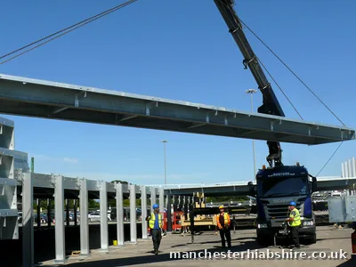 HIAB lifting a long galvanised steel beam into a canopy frame with three crew