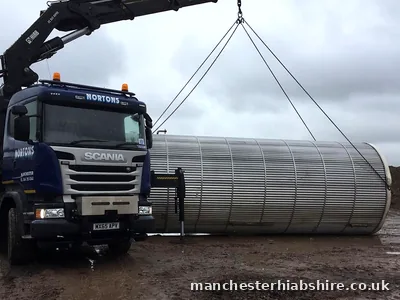 Large stainless tank slung from the lorry mounted crane on a muddy site